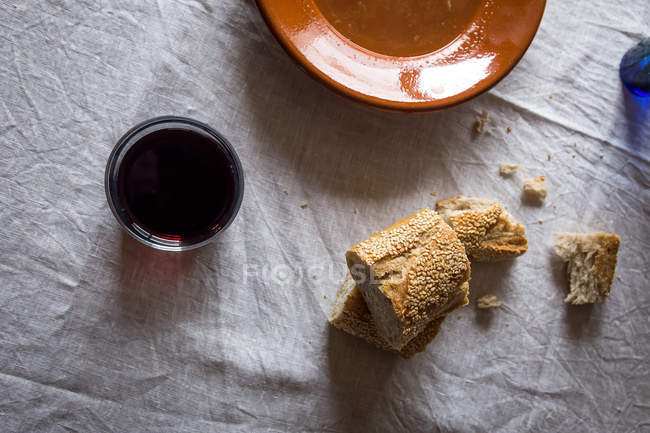 Вид зверху на склянку вина і скибочки хліба біля порожньої теракотової тарілки на рваній скатертині — стокове фото