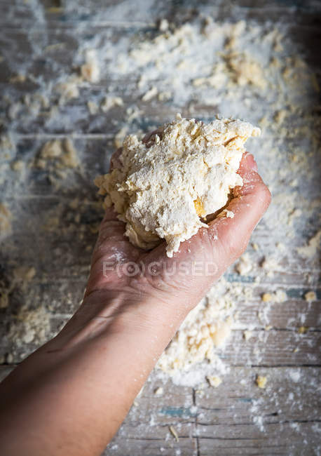 Above view of hand with lump of dough over rustic table with flour — Stock Photo