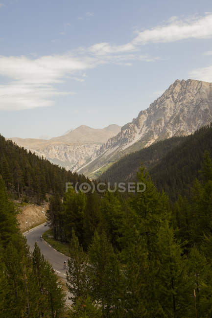 Живописный пейзаж с силуэтами велосипедистов на извилистой дороге в горах — стоковое фото