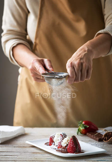 Partie médiane de la femelle versant du sucre en poudre avec passoire sur les fraises fraîches dessert sur assiette — Photo de stock