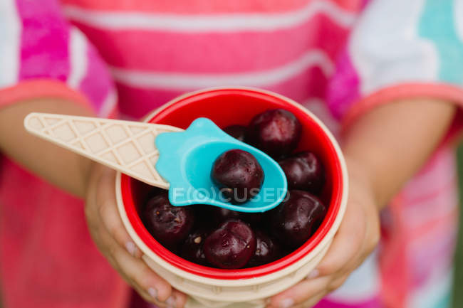 Primo piano di bambina che tiene ciotola di ciliegie fresche con cucchiaio di plastica — Foto stock