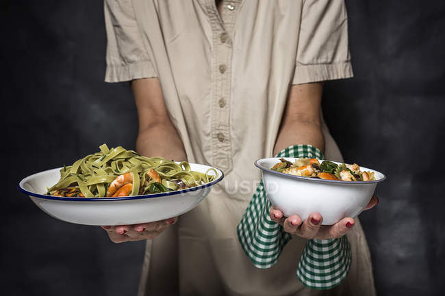 Midsection of woman holding plates of italian green tagliatelle with seafood — Stock Photo