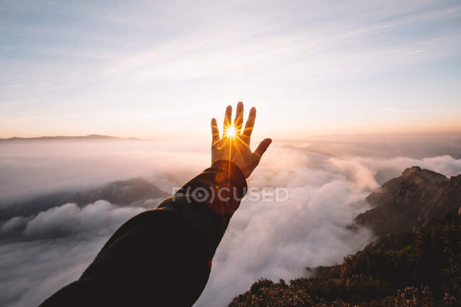 Hand stretched to sunset closing sun on background of clouds. — Stock Photo