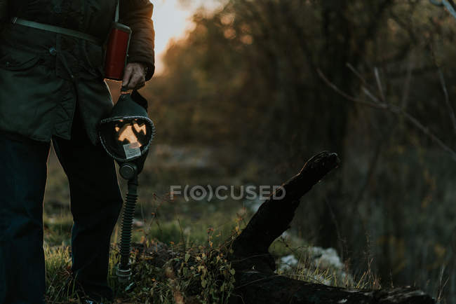 Low section view of man walking at rural field and holding gas mask in hands — Stock Photo