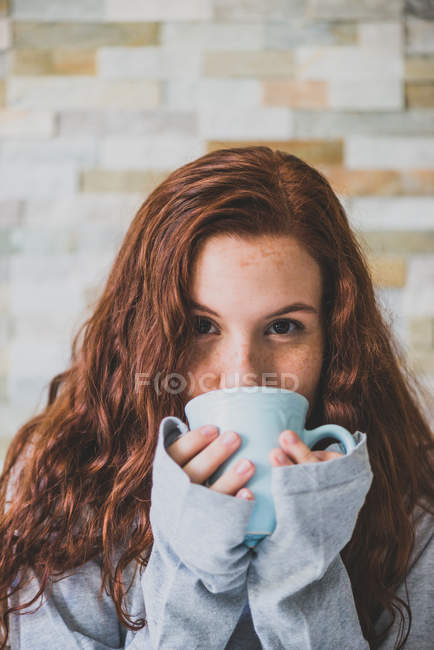 Дівчина п'є з блакитного горнятка і дивиться на камеру — стокове фото