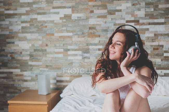 Chica sentada en la cama y escuchando música - foto de stock
