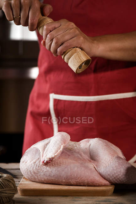 Primer plano de la mujer rociando pollo crudo con pimienta - foto de stock