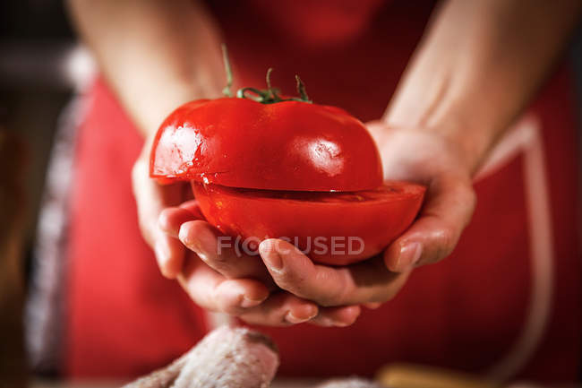 Primer plano de las manos femeninas sosteniendo tomate fresco cortado a la mitad - foto de stock