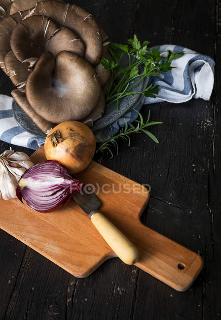 Vista de ángulo alto de tablero de madera con cebolla y cuchillo cerca de setas pleurotus en toalla - foto de stock