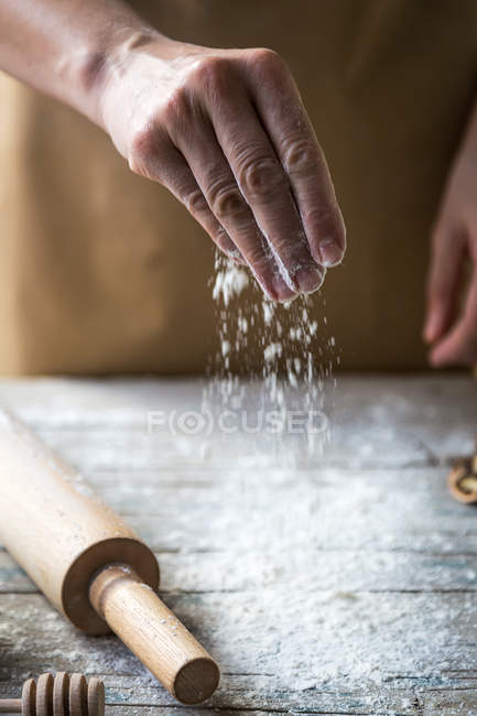 Vista de cerca de la mano verter harina en la mesa de madera rural - foto de stock