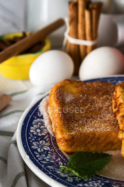 Крупный план сладких тостов на декоративной тарелке над яйцами и коричными палочками на заднем плане — стоковое фото