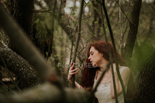 Чувственная девушка в белом платье позирует на лесах и трогает шею — стоковое фото