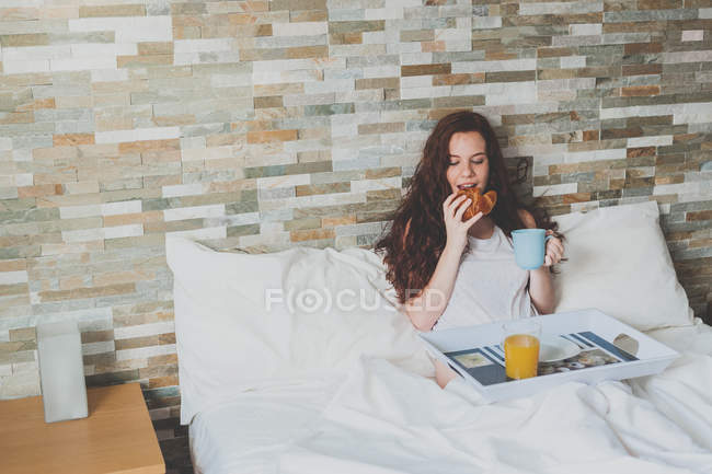 Mujer pelirroja joven desayunando en la cama - foto de stock