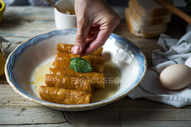 Close up view of female hand putting mint leaves on plate with fried honey dough tubes — Stock Photo