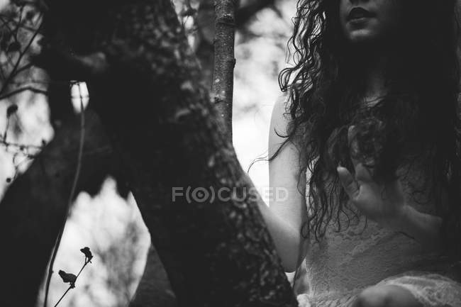 Crop girl in white dress sitting on branches — Stock Photo