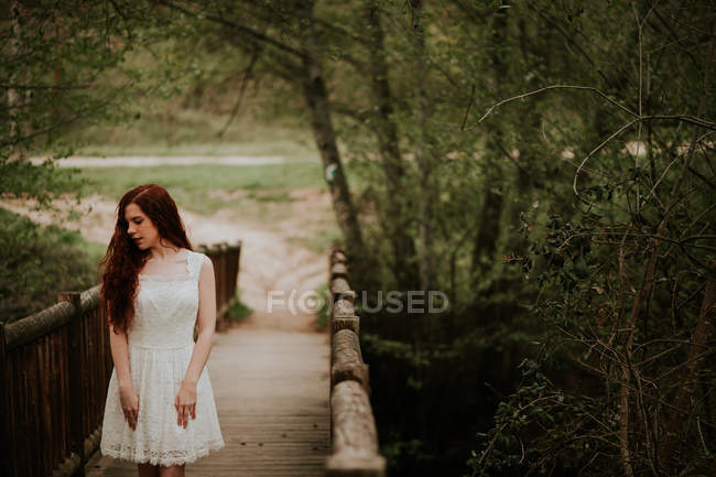 Chica jengibre sensual posando en vestido blanco en puente de madera - foto de stock