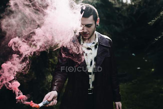 Young man standing in forest and holding burning smoke candle. — Stock Photo
