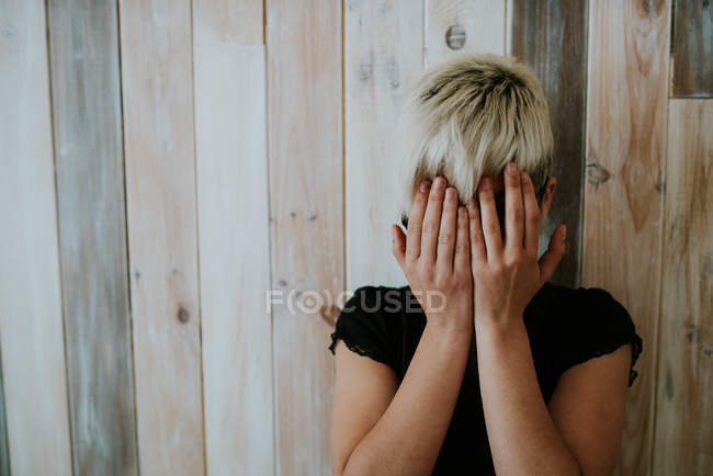 Дівчина з коротким світлим волоссям ховається обличчям руками — стокове фото