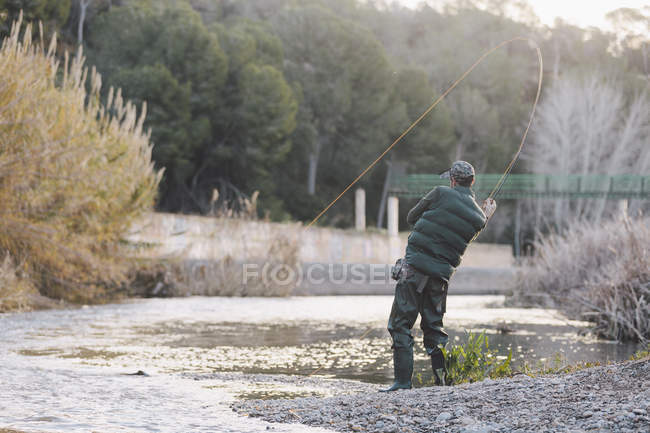 Vista trasera de la pesca pesquera con caña en el río en el día soleado - foto de stock