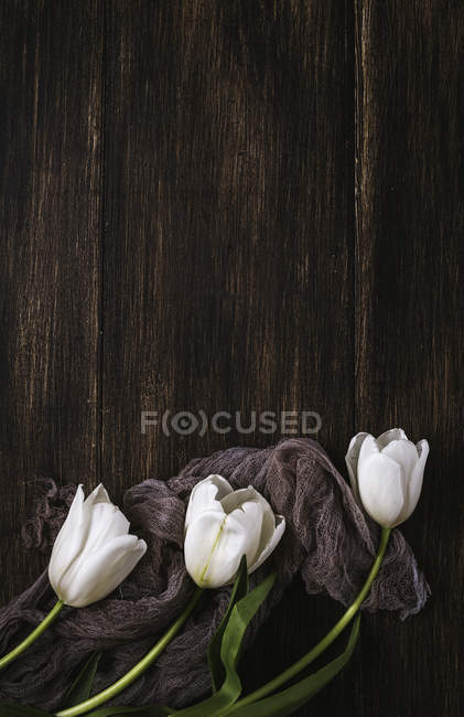 Цветочный фон с белыми тюльпанами и глянцевой тканью на деревянном фоне — стоковое фото
