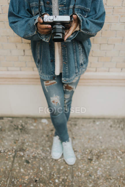 Abgeschnittenes Bild einer Frau, die sich an die Wand lehnt und eine Analogkamera in der Hand hält — Stockfoto