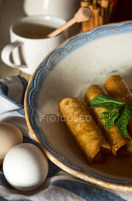 Обрезка тарелки с трубками из сладкого теста и мятными листьями на полотенце с яйцами — стоковое фото