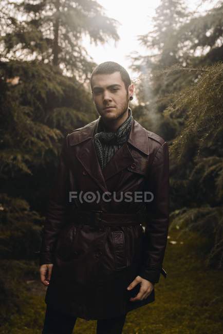Ritratto di uomo che indossa un cappotto di pelle in posa tra i boschi e guarda la macchina fotografica — Foto stock
