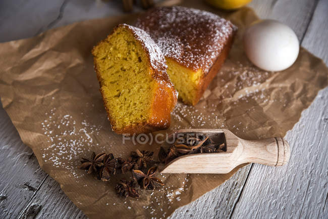 Still life of sliced lemon cake with scoop of anise stars on bakery paper over rural wooden table — Stock Photo