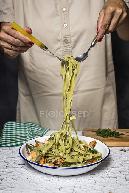 Sezione centrale della donna che avvolge tagliatelle verdi italiane sulla forchetta — Foto stock