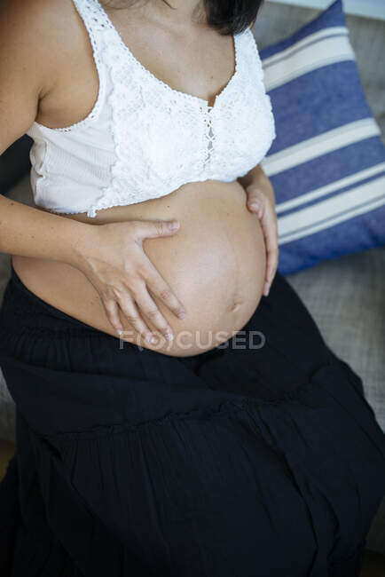 Неузнаваемая беременность держит её живот. Закрыть вид на голый животик. — стоковое фото