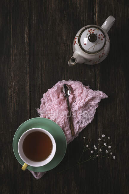 Tasse Tee mit floralem Hintergrund mit roten und weißen Tulpen und Gänseblümchen und grünen Blättern auf braunem Hintergrund. Flache Lage, Draufsicht — Stockfoto