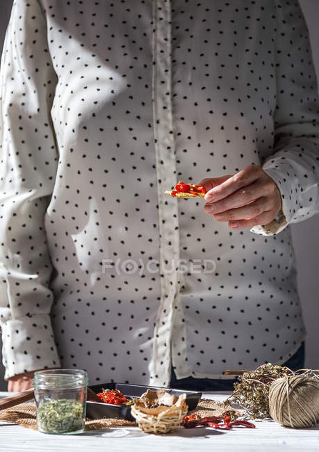 Mid section of female holding italian snack with dried tomatoes over table with kitchenware — Stock Photo