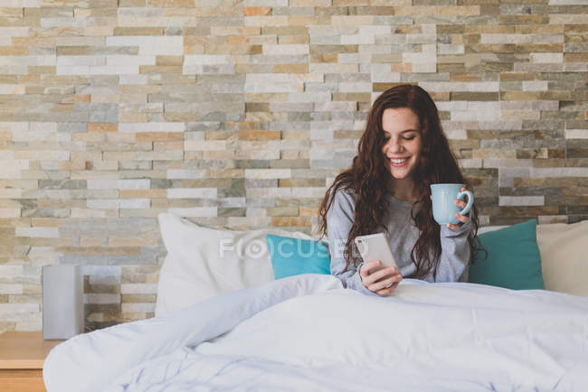 Девушка лежит на кровати и использует смартфон — стоковое фото