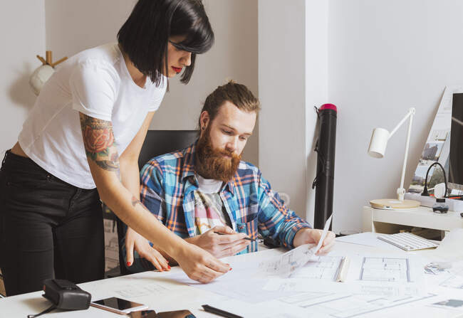 Portrait of male and female architects discussing blueprints in office — Stock Photo