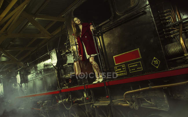Молода жінка стоїть на великому чорному потязі і тримає поручень . — стокове фото