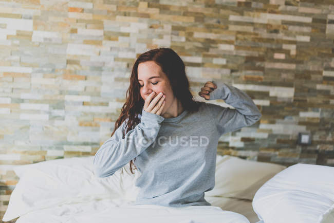 Girl in pajama yawns and covers face with arm — Stock Photo