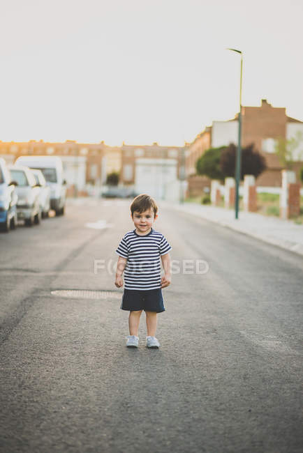 Portrait of cute little boy smiling at camera while standing on asphalt road in suburb — Stock Photo
