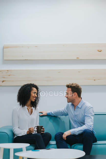 Vista de homem e mulher sentados no sofá azul, olhando um para o outro, conversando e rindo. Espaço de cópia — Fotografia de Stock