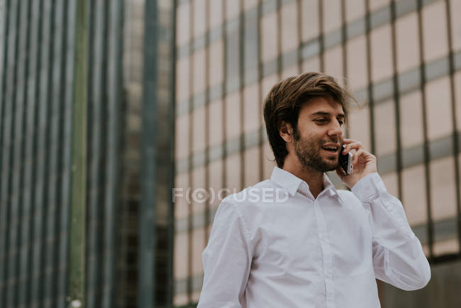Portrait of brunette businessman in white shirt talking on smartphone at downtown area — Stock Photo
