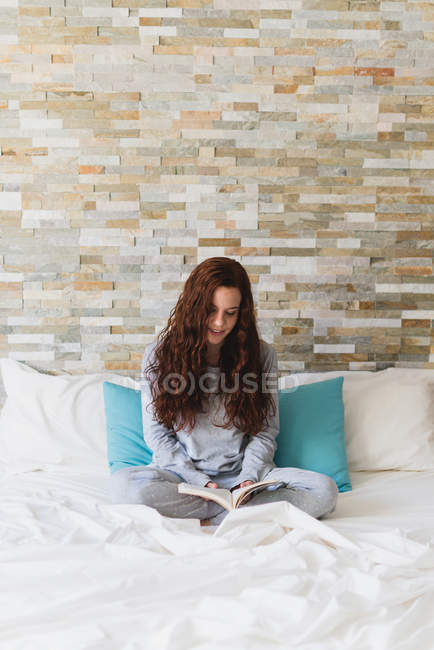 Chica sentada en la cama y leyendo libro - foto de stock