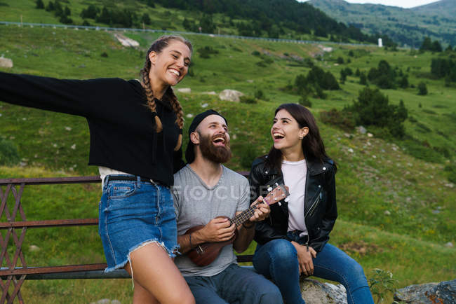 Homem cantando com mulheres enquanto joga ukulele no prado verde . — Fotografia de Stock
