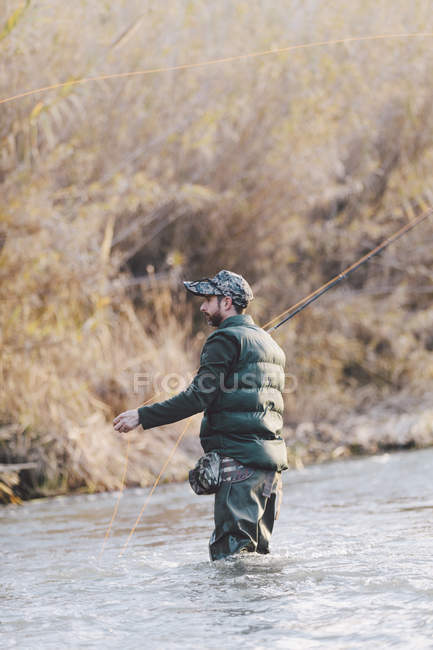 Vista lateral do homem de pé no rio e pesca com vara no dia de outono — Fotografia de Stock