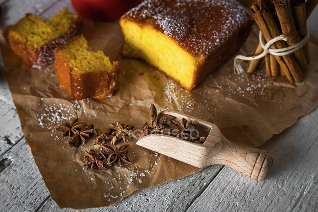 Vue grand angle des tranches de gâteau au citron sur du papier de boulangerie avec une cuillère d'étoiles d'anis et une pile de bâtonnets de cannelle sur une table de cuisine rustique — Photo de stock
