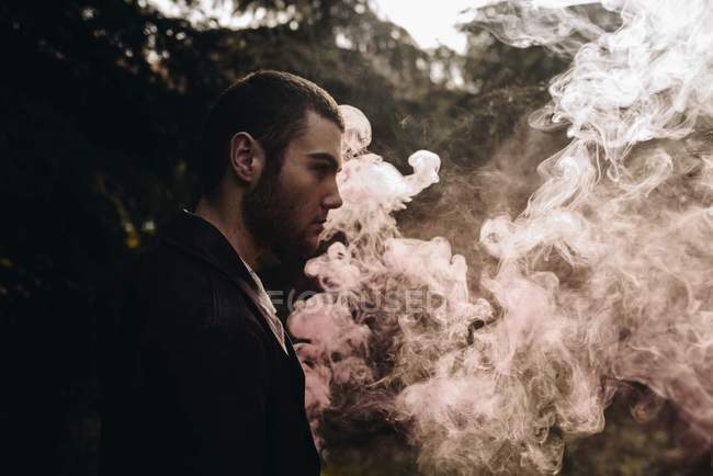Side view of man standing in pink smoke among woods — Stock Photo
