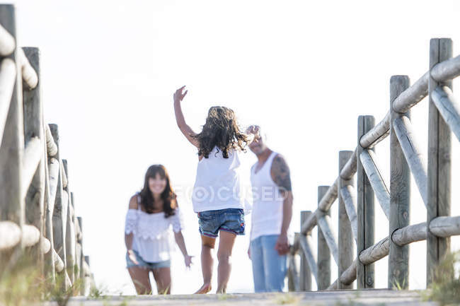 Rear view of girl running on board walk to parents — Stock Photo
