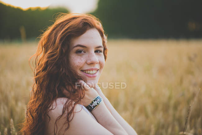 Портрет привлекательной рыжей девушки, смотрящей на камеру на ржаном поле на закате — стоковое фото