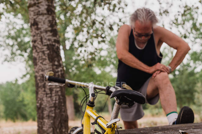 Vista frontal de seniorman alongamento pernas no parque perto de bicicleta — Fotografia de Stock