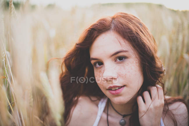 Retrato de cerca de la joven pelirroja sentada en el campo de centeno y mirando a la cámara - foto de stock
