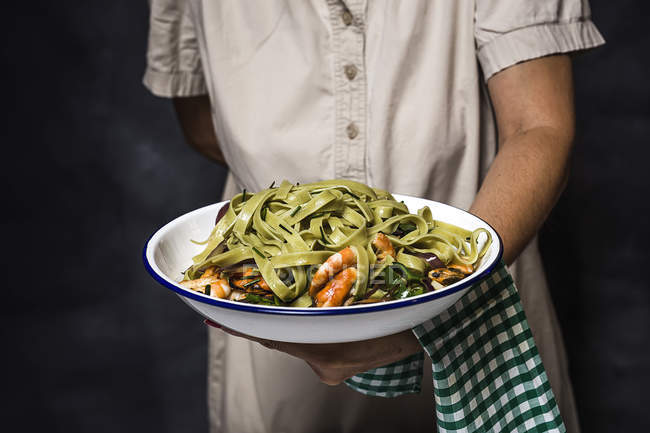 Midsection of woman giving plate of italian green tagliatelle with seafood — Stock Photo