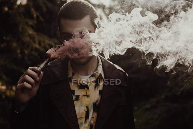 Портрет человека, прячущего лицо в дыму от дымовой свечи в руке — стоковое фото